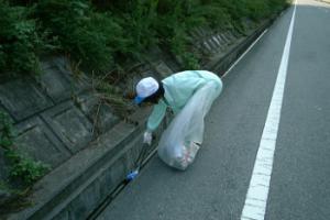 道路脇に捨てられたごみを火ばさみで拾う風景