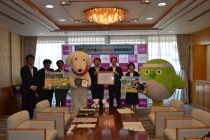貴賓室でイオン贈呈者・WAONくん・知事・生活環境部長・めじろんが並んで寄附金目録や感謝状を持っている